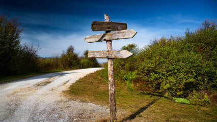 An old wooden road sign stands next to an old dirt road.