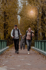 Mom and dad holding babys hands and having fun in the autumn park on the bridge