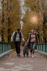 Mom and dad holding babys hands and having fun in the autumn park on the bridge