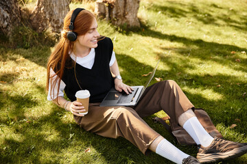 A young man relaxes on the grass with a laptop, immersed in his work, and sipping coffee.