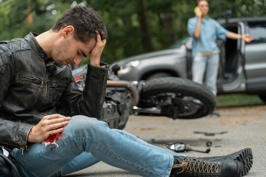 Motorcyclist sits on the asphalt near motorcycle, after road accidents with car. Broken and wrecked motorcycle on road
