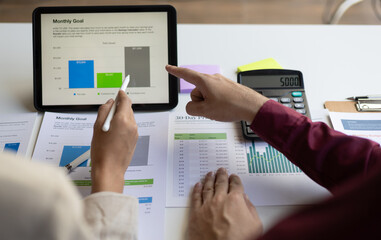 Meetings discuss business situations by analyzing financial charts in company reports on digital tablets to analyze strategies and plan new investment projects to increase profits.