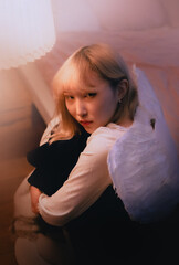 A beautiful Asian woman, with white wings, sits alone, like an angel, in the evening. She is...
