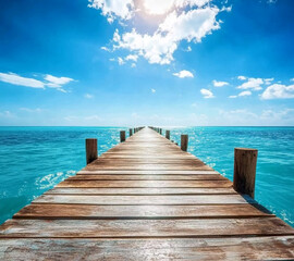 A wooden pier is in front of a beautiful blue ocean. The sky is cloudy, but the water is calm and clear.
