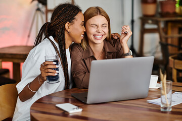 A happy moment unfolds as an African American woman shares a warm smile with her girlfriend at a bustling cafe.