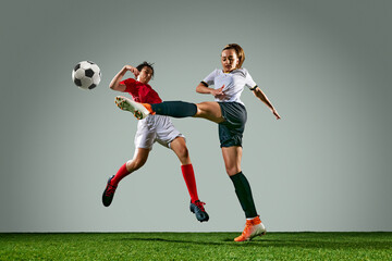 Competitive moment between two female soccer players in dynamic motion, kicking ball with focus. Rainy training session. Concept of sport, action, competition, game. Copy space