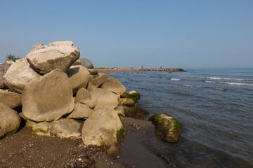 Large rocks on the shore of the Caspian Sea. In the background fishermen stand on the shore and fish with a rod.