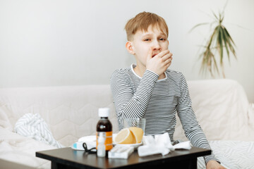 Sick little kid teen boy sits on bed at home and and sneezes. Flu season. Healthcare concept.