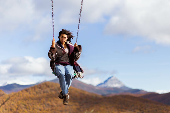 Young woman swinging on the giant swing in Ria&ntilde;o, Le&oacute;n, Spain, surrounded by a stunning backdrop of the 'Fiords of Le&oacute;n.' As she swings out over the breathtaking landscape, vast mountains and the calm