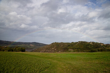 Obraz premium Idyllic valley view with rolling hills and a colorful rainbow, creating a serene landscape scene in the countryside.