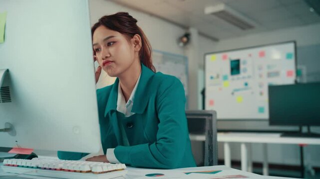 Asian businesswoman sitting at her desk is having a headache while working on her computer. She is feeling stressed and tired