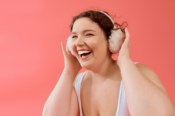 Fototapeta premium A cheerful plus size woman smiles broadly while embracing her love for music on a bright background.