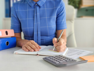 Business lady writing in a notebook with a pen and calculating financial reports in the office