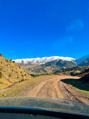 View of snow-capped peaks and mountain slopes from a car window during an autumn journey in Kyrgyzstan.