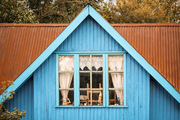 Bright blue wooden cottage window, adorned with lace curtains and sculpted objectsin Ancud, Chile, exemplifies the traditional aesthetics of this region.