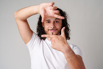 A young man with curly hair framing his face and making a gesture as if capturing a moment against...