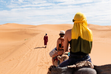 Turistas en camello por el desierto de Merzouga con un guía amazigh