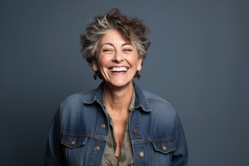 Portrait of a joyful woman in her 50s wearing a rugged jean vest over blank studio backdrop