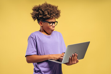 Portrait excited, amazed African American boy with curly hairstyle wearing eyeglasses holding laptop
