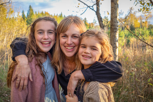 Close-up portrait of a mother embracing her two daughters and smiling at the camera in a rural setting in Beckwith Township at Carleton Place in the Ottawa Valley; Ontario, Canada