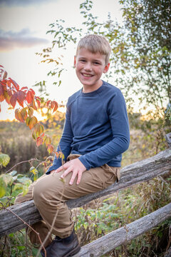 Close-up portrait of a boy sitting on a wooden fence, smiling at the camera in a rural setting in the Fall, Beckwith Township at Carleton Place in the Ottawa Valley; Ontario, Canada