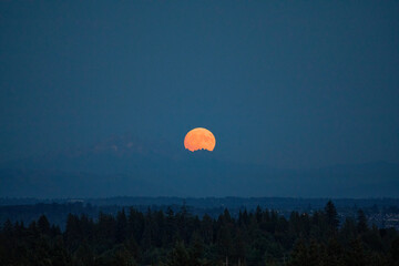 Harvest moon behind the mountains in Surrey, BC, Canada; Surrey, British Columbia, Canada