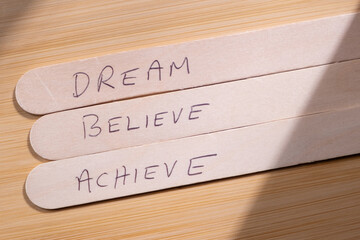 Success concept background. Phrase Dream Believe Achieve written on wooden popsicle sticks placed...