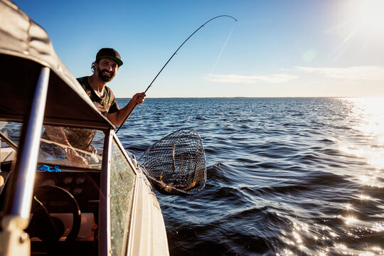 Man catches a fish from a boat during time on a lake; Alberta Beach, Alberta, Canada