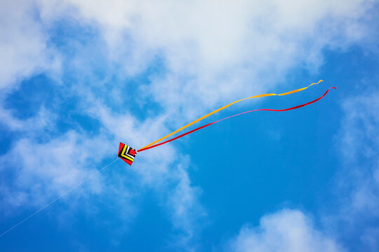 Kite with red and yellow tails flying in a blue sky with clouds: Northumberland, England