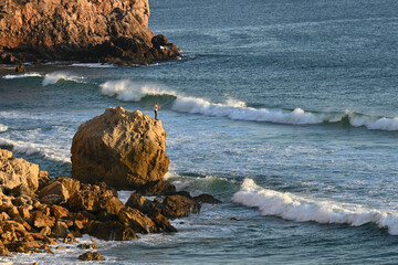 Man fishing from a large boulder off Praia do Zavial in the North Atlantic, in the Algarve region of Portugal; Raposeira, Faro, Portugal