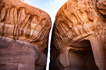 Huge rock formations and a tomb silhouetted against a bright sky in Hegra near Al Ula Saudi Arabia