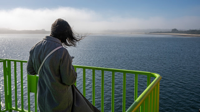 Female tourist using her smart phone as she rides a ferry into the fog across the Sado River from Setubal to Costa de Gale in Portugal; Portugal