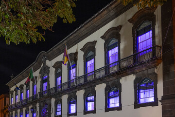 Building windows glowing with blue light and flags along the balconet; Funchal, Madeira, Portugal