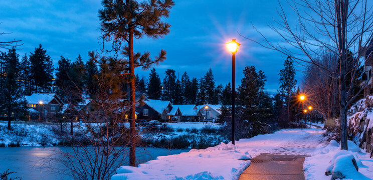 Lakeside housing development in winter with lamp posts lighting the footpath at twilight; Kelowna, British Columbia, Canada