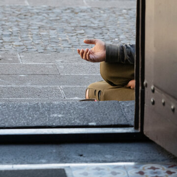 Beggar sits outside a doorway holding out their hand; Camara de Lobos, Madeira, Portugal