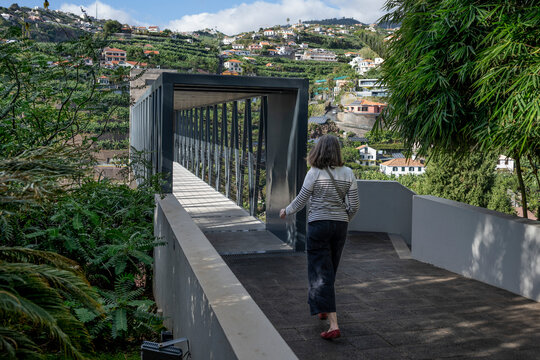 Woman walks towards an elevated walkway in the town of Ponta do Sol on the island of Madeira in Portugal; Ponta do Sol, Madeira, Portugal