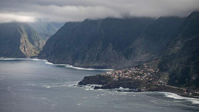 View from Eira da Achada viewpoint of the rugged cliffs along the coastline under storm clouds and houses at Ribeira da Ja on the island of Madeira, Portugal; Ribeira da Janela, Madeira, Portugal
