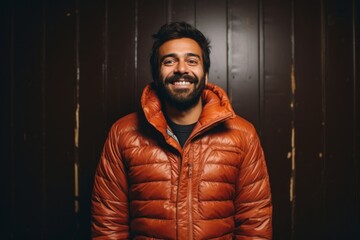 Portrait of a smiling indian man in his 30s sporting a quilted insulated jacket isolated in bare monochromatic room