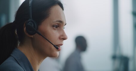 Female helpdesk specialist working in modern call center office: Close up portrait of Caucasian hotline operator using headset to talk with client, providing online technical support for customer.