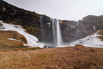 Obraz premium Powerful waterfall flowing from snowy cliffs in iceland