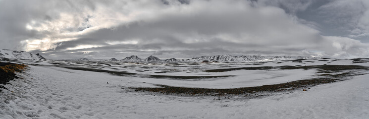 Person walking in snow covered landscape with mountains and cloudy sky