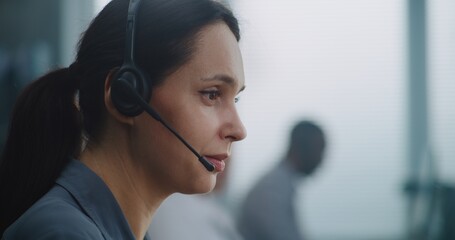 Female helpdesk specialist working in modern call center office: Close up portrait of Caucasian hotline operator using headset to talk with client, providing online technical support for customer.