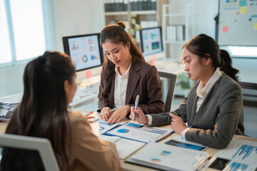 Three asian businesswomen are collaborating on a project, analyzing financial reports, and discussing strategies in a modern office environment, working together to achieve business success