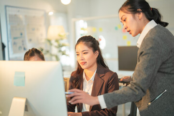 Three asian businesswomen are working together in modern office using desktop computer, discussing and collaborating on a project