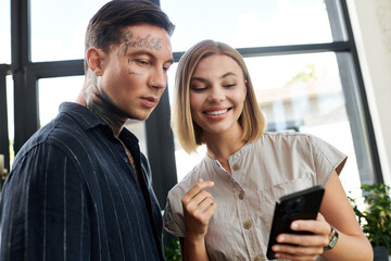 Two colleagues engage with enthusiasm, laughing and discussing on a mobile phone in the office.