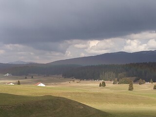 Green and yellow hilly landscape under cloudy ceiling with sun breaking through