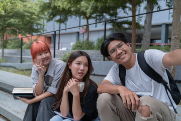 Three happy asian students taking a selfie on campus during break time, enjoying the fun and casual university life together, capturing memories with smartphones