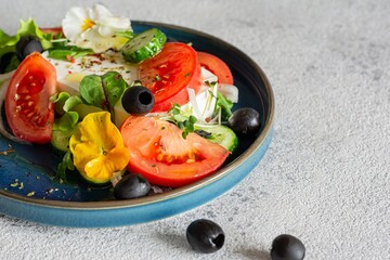 Appetizing salad with feta cheese, fresh vegetables (tomatoes, cucumbers, onions), crispy lettuce, microgreens and violet flowers. Non-standard serving of Greek salad.