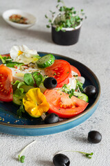 Appetizing salad with feta cheese, fresh vegetables (tomatoes, cucumbers, onions), crispy lettuce, microgreens and violet flowers. Non-standard serving of Greek salad.