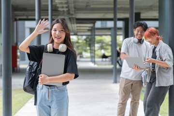 Young asian woman happily waves with a laptop, surrounded by friends in a university campus. They share knowledge and skills, connecting through technology in a cheerful manner